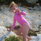 A young girl climbing a rock face wearing a UV Protective Long Sleeve Swimsuit Pink Starfish while holding a feather.